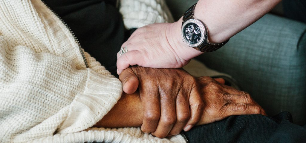 A nurse and resident hold hands in a skilled nursing facility